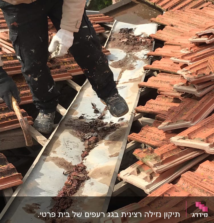 אדם מנקה תעלה על גג רעפים עם כלי עבודה